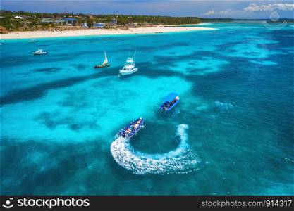 Aerial view of boats and floating water scooter in blue sea at sunset in summer. Holiday in Indian ocean, Zanzibar, Africa. Top view of jet ski in motion. Tropical seascape with moving motorboat