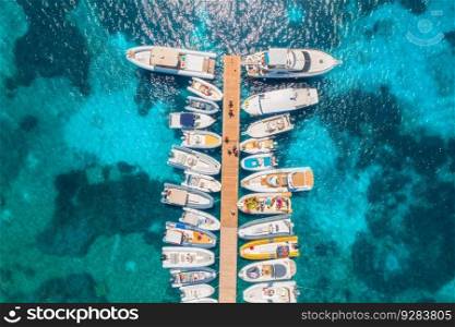 Aerial view of boats and luxure yachts in dock at sunset in summer in Sardinia, Italy. Colorful landscape with sailboats and motorboats in sea bay, jatty, clear blue sea. Top view of harbor. Travel