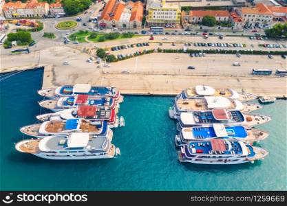 Aerial view of boats and luxury yachts in port at sunset. Summer landscape with buildings with orange roofs, motorboats in harbor, clear blue sea. Beautiful architecture. View from above. Travel