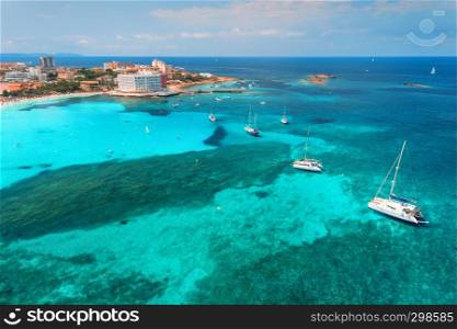 Aerial view of boats and luxury yachts in the clear sea at sunset in summer in Mallorca, Spain. Colorful seascape with lagoon, azure water, sandy beach, blue sky. Balearic islands. Top view. Travel