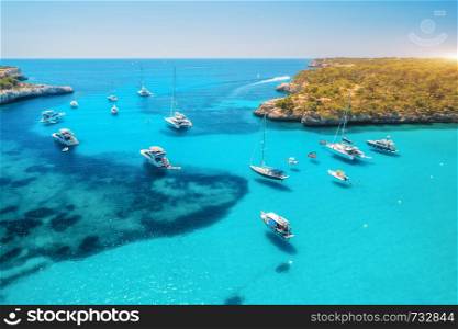 Aerial view of boats and luxury yachts in transparent sea at sunny day in summer in Mallorca, Spain. Colorful landscape with bay, azure water, green trees, blue sky. Balearic islands. Top view. Travel