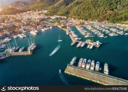 Aerial view of boats and yachts at sunset in Turkey. Colorful landscape with boats in marina bay, sea, mountains, forest, blue sky. Top view from drone of harbor with luxury yacht, sailboat. Travel. Aerial view of boats and yachts at sunset