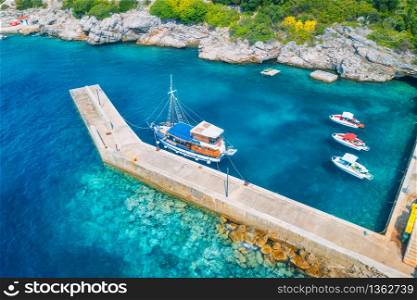 Aerial view of boats and yachts in clear blue water, pier, rocks at sunset in summer. Top view from drone of boat, green trees. Travel. Tropical landscape with water scooters, sea. View from above