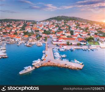 Aerial view of boats and yachts in port and city on the mountain at sunset. Summer landscape with buildings, motorboats in harbor, blue sea and colorful sky. Beautiful architecture. Top view. Travel