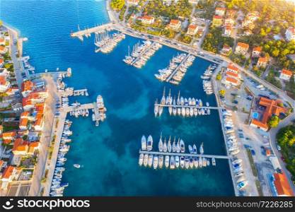 Aerial view of boats and yachts in port in beautiful old city at sunset in Croatia in summer. Landscape with buildings with orange roofs, motorboats in harbor, clear blue sea, cars, road. Top view
