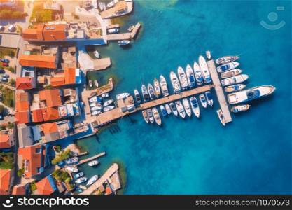 Aerial view of boats and yachts in port in old city at sunset. Summer landscape with buildings with orange roofs, motorboats in harbor, clear blue sea. Beautiful architecture. View from above. Travel