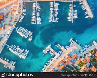Aerial view of boats and yachts in port in old city at sunset. Summer landscape with houses with orange roofs, motorboats in harbor, clear blue sea, cars on the road. Beautiful architecture. Top view