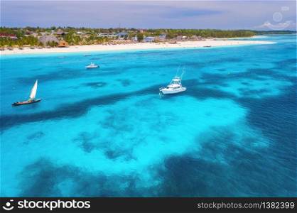 Aerial view of boats and yachts on tropical sea coast with sandy beach at bright sunny day in summer. Indian Ocean in Africa. Landscape with boat, palm trees, clear blue water, sky. View from above. Aerial view of boats and yachts on tropical sea coast in summer