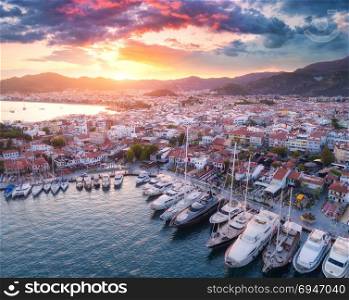 Aerial view of boats and yahts and beautiful architecture at sunset in Marmaris, Turkey. Landscape with boats in marina bay, sea, city, mountains. Top view from drone of harbor with yacht and sailboat. Aerial view of boats and yahts and beautiful architecture at sunset