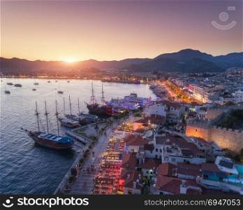 Aerial view of boats and yahts and beautiful architecture at sunset in Marmaris, Turkey. Landscape with boats in marina bay, sea, city, mountains. Top view from drone of harbor with yacht and sailboat. Aerial view of boats and yahts and beautiful architecture at sunset