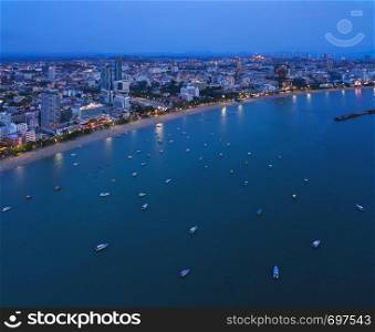 Aerial view of boats in Pattaya sea, beach at night, and urban city with blue sky for travel background. Chon buri Province, Thailand.