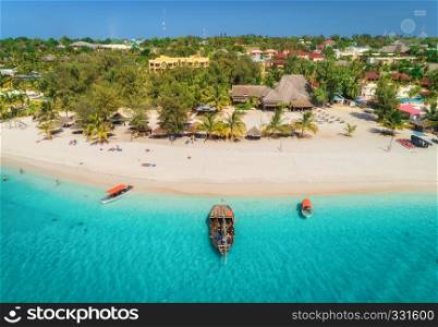 Aerial view of boats on tropical sea coast with sandy beach at sunny day. Summer holiday on Indian Ocean, Zanzibar, Africa. Landscape with boat, palm trees, transparent blue water, hotels. Top view