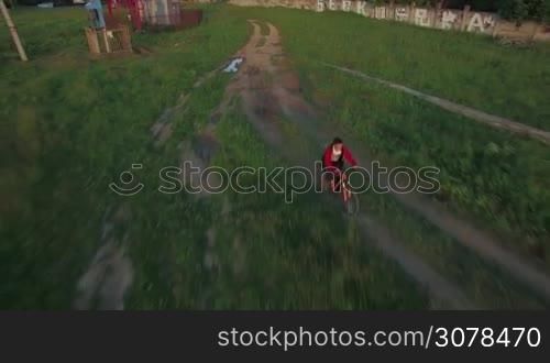 Aerial view of boy riding a bike along countryside road between agricultural fields at summer, Russia