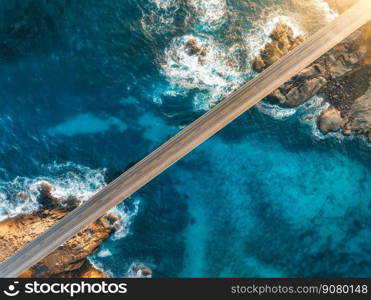 Aerial view of bridge, sea with waves and stones at sunset in Lofoten Islands, Norway. Landscape with beautiful road, transparent blue water, rocks. Top view from drone of highway in summer. Transport