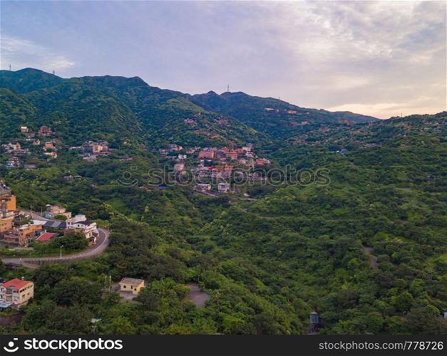 Aerial view of buildings in Jiufen village on mountain hill with green natural forest trees in rural area of New Taipei City, Taiwan