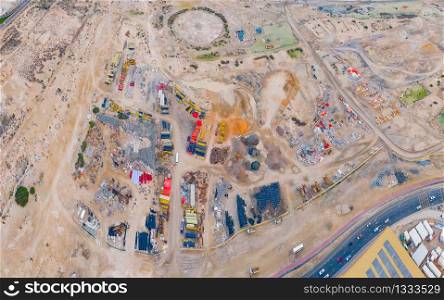 Aerial view of busy industrial construction site workers with cranes working. Top view of development high rise architecture building with sand desert in Dubai City, UAE.
