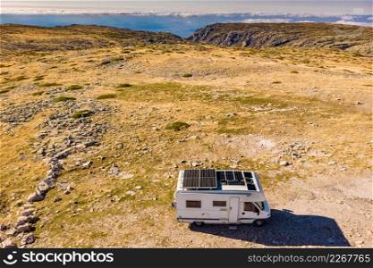 Aerial view of camper with a lot of solar photovoltaic panels on roof camping in mountain nature. Renewable free energy. Elecrticity on caravan holidays.. Caravan solar panels on roof camp in mountains. Aerial view