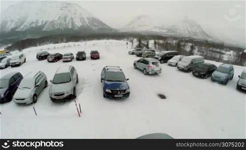 Aerial view of car driving out the outdoor parking area in winter day and moving along the road covered with snow