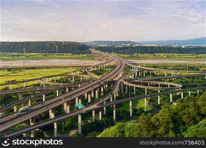 Aerial view of cars driving on complex highway or freeway with trees. Bridge roads or streets in structure of architecture and transportation concept. Top view. Urban city, Taichung at sunset, Taiwan.