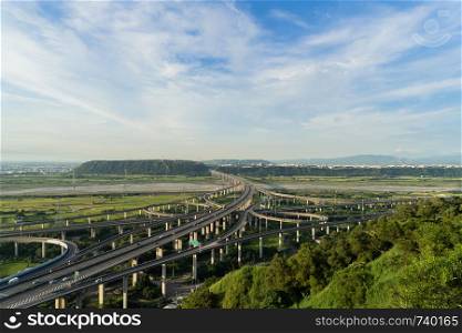 Aerial view of cars driving on complex highway or freeway with trees. Bridge roads or streets in structure of architecture and transportation concept. Top view. Urban city, Taichung at sunset, Taiwan.