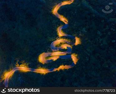 Aerial view of cars driving on curved, zigzag road or street on mountain hill with natural forest trees in rural area of New Taipei City, Taiwan at night