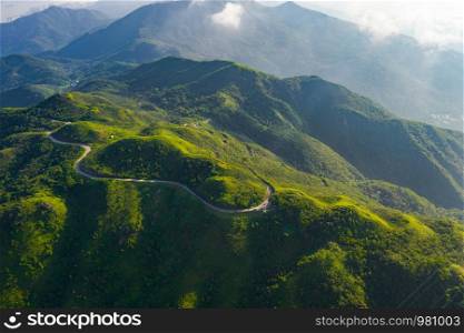 Aerial view of cars driving on curved, zigzag road or street on mountain hill with green natural forest trees in Kowloon City, Hong Kong, Republic of China.