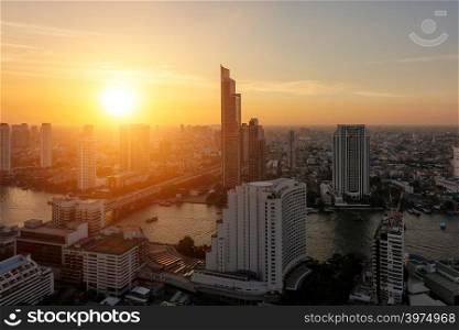 Aerial view of Chao Phraya River at sunset. Sun goes down in Bangkok Downtown. Financial district and business centers in smart urban city in Asia. Skyscraper and high-rise buildings at sunset.