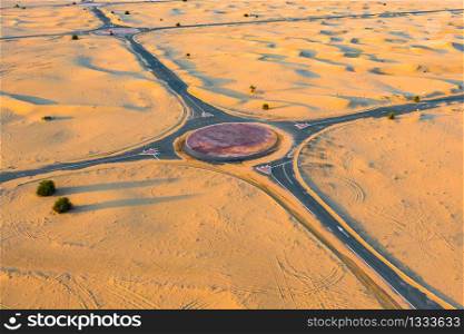 Aerial view of circle roundabout, half desert road or street with sand dune in Dubai City, United Arab Emirates or UAE. Natural landscape background at sunset time. Famous tourist attraction.