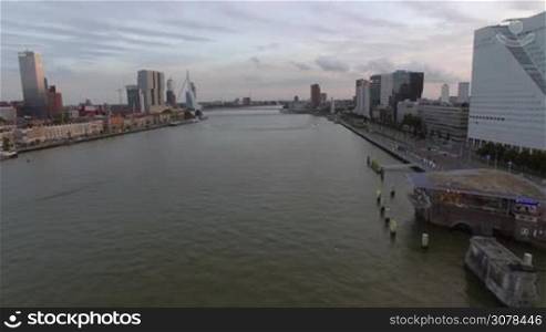 Aerial view of cityscape with modern buildings, skyscrapers, office center, flight along the Rotte river against cloudy sky, Rotterdam, Netherlands