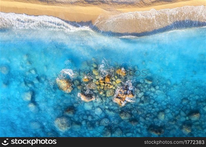 Aerial view of clear blue sea with waves, stones and rocks, empty sandy beach at sunset. Summer in Oludeniz, Turkey. Tropical seascape with azure water. Top view of sea coast. Nature background
