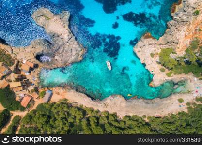 Aerial view of clear sea with blue water, sandy beach, rocks, green trees, yachts and boats in sunny morning in summer. Travel in Mallorca, Balearic islands, Spain. Top view. Colorful landscape