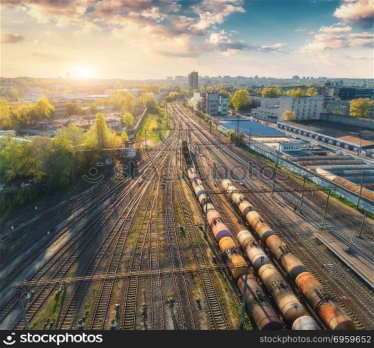 Aerial view of colorful freight trains on railway station. Wagons with goods on railroad. Cargo trains. Heavy industry. Industrial scene with trains, city buildings and blue sky at sunset. Top view . Aerial view of colorful freight trains on railway station. Aerial view of colorful freight trains on railway station