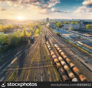 Aerial view of colorful freight trains on railway station. Wagons with goods on railroad. Cargo trains. Heavy industry. Industrial scene with trains, city buildings and blue sky at sunset. Top view . Aerial view of colorful freight trains on railway station. Aerial view of colorful freight trains on railway station