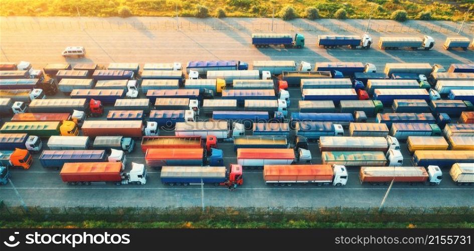 Aerial view of colorful trucks in terminal at sunrise in summer. Top view of logistic center. Heavy industry. Transportation. Cargo transport, shipping. International trucking. View from above of cars
