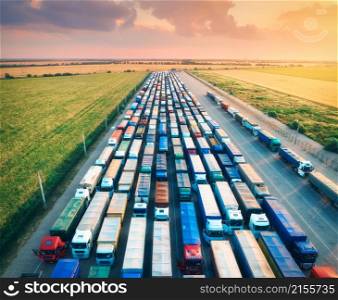 Aerial view of colorful trucks in terminal at sunrise in summer. Top view of logistic center. Heavy industry. Transportation. Cargo transport, shipping. International trucking. View from above of cars