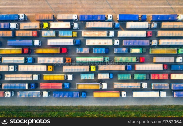 Aerial view of colorful trucks in terminal at sunset in summer. Top view of logistic center. Heavy industry. Transportation. Cargo transport, shipping. International trucking. View from drone of truck