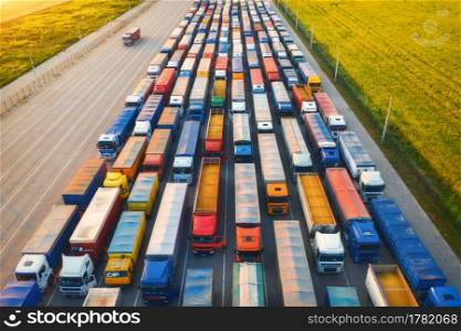 Aerial view of colorful trucks in terminal at sunset in summer. Top view of logistic center. Heavy industry. Transportation. Cargo transport, shipping. International trucking. View from drone of truck