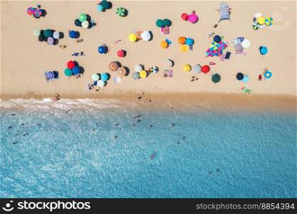 Aerial view of colorful umbrellas on sandy beach, people in blue sea at bright sunny day in summer. Beach, Sardinia, Italy. Tropical landscape with turquoise water. Travel and vacation. Top view