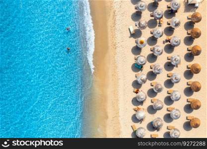 Aerial view of colorful umbrellas on sandy beach, people in blue sea at summer sunny day. Sardinia, Italy. Tropical background. Seascape. Travel and vacation. Top drone view of ocean with waves