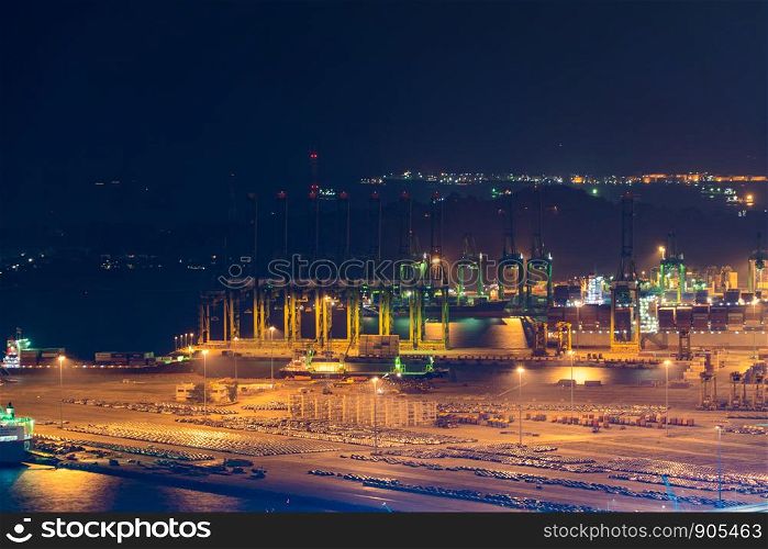 Aerial view of container cargo ship in the export and import business and logistics international goods in urban city. Shipping to the harbor by crane in Singapore City at night.
