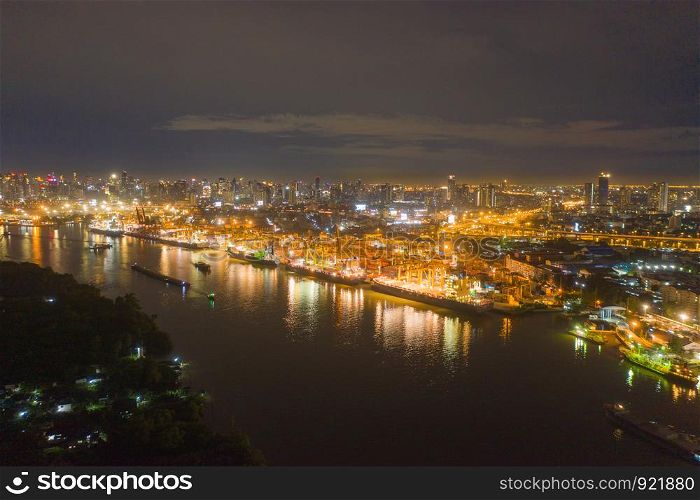 Aerial view of container cargo ship in the export, import business, logistics and transportation. International goods in urban city. Shipping to the harbor by crane in Bangkok City, Thailand at night.