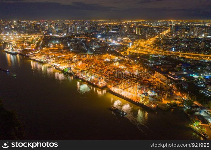Aerial view of container cargo ship in the export, import business, logistics and transportation. International goods in urban city. Shipping to the harbor by crane in Bangkok City, Thailand at night.