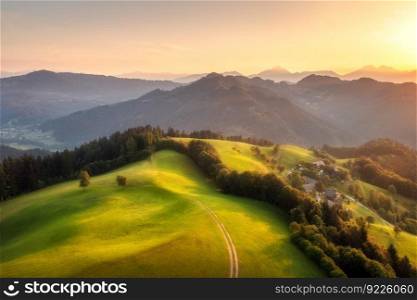 Aerial view of country road in green hills at sunset in summer. Top view from drone of rural dirt road, meadows , mountains, forest in spring. Beautiful landscape with trail, trees, grass. Slovenia
