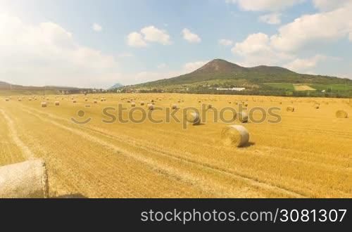 Aerial view of cropped wheat field with bales of hay in the countryside with a beautiful view of the mountain on a sunny day.