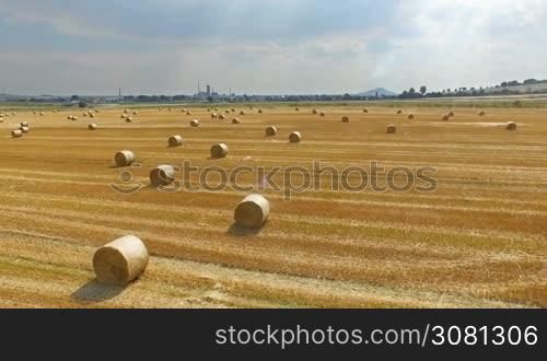 Aerial view of cropped wheat field with bales of hay in the countryside. View of the highway with driving lorryes on a sunny day.