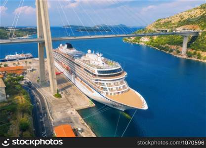 Aerial view of cruise ship and beautiful bridge in Dubrovnik, Croatia. Top view of large ship and road at sunset. Summer landscape with harbor, mountain, blue sea and green trees. Cruise liner in port