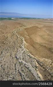 Aerial view of desert with lake and mountains in background.