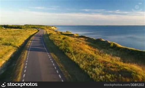 Aerial view of driving black car on the road along the cliff near the sea in summer at sunset. Beautiful cloudy blue sky on the sunset.