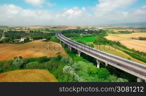 Aerial view of driving vehicles by the highway between fields and rural settlements by summer sunny day in Tuscany, Italy
