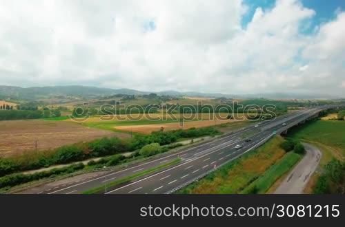 Aerial view of driving vehicles by the highway between yellow and green grass. Aerial view of fields and rural settlements by summer sunny day in Tuscany, Italy
